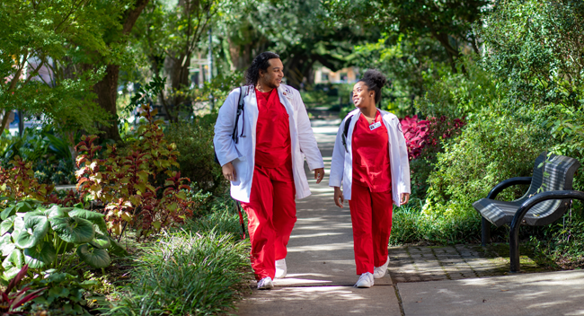 Two UL Lafayette nursing students walking underneath a canopy of oak trees on campus