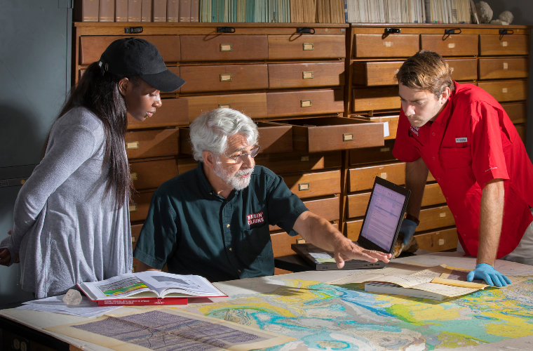 A professor and two students working with the map collection in the Louisiana Room on campus.