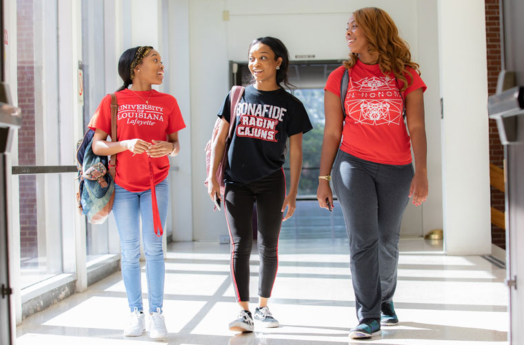 Three UL Lafayette students talking and walking down a brightly lit hallway