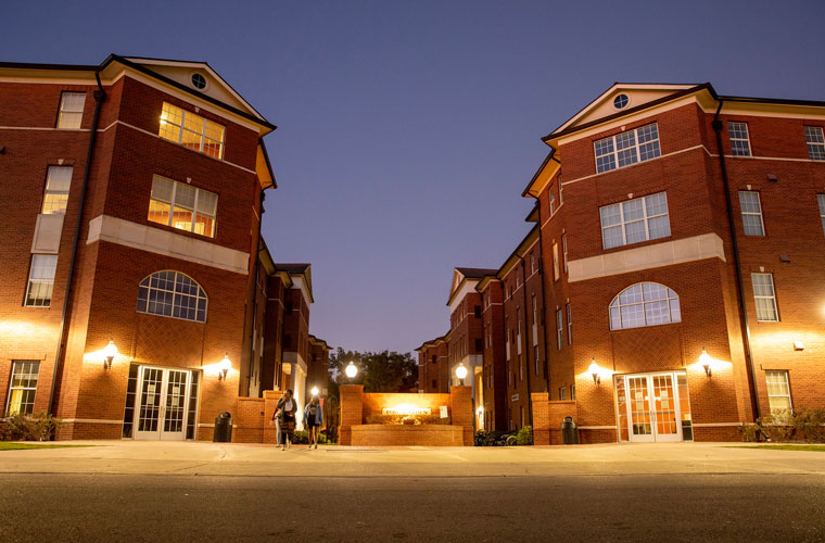 Rose Garden dorms in the early evening with lights and students walking on UL Lafayette campus