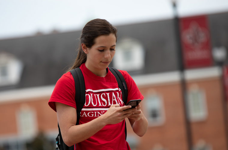 UL Lafayette student walking through the Quad while looking at her phone