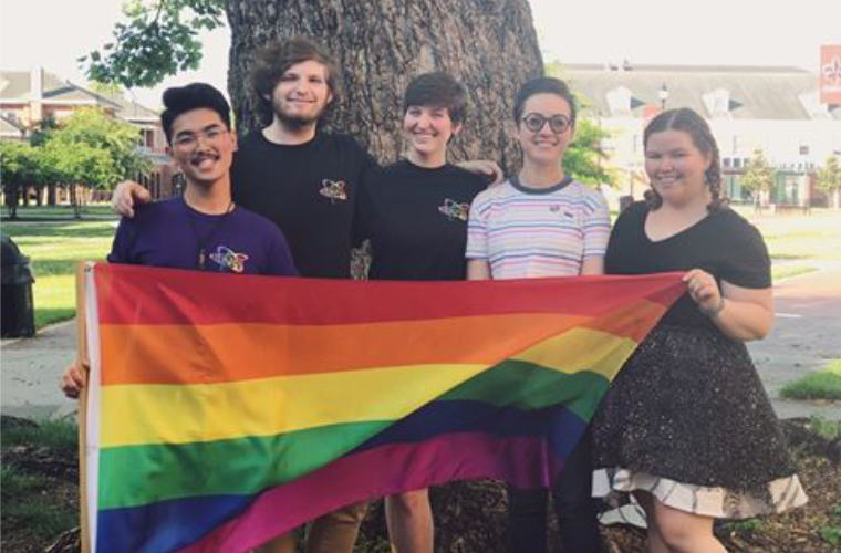 A group of students in an LGBTQ+ club holding a rainbow flag on campus at UL Lafayette.