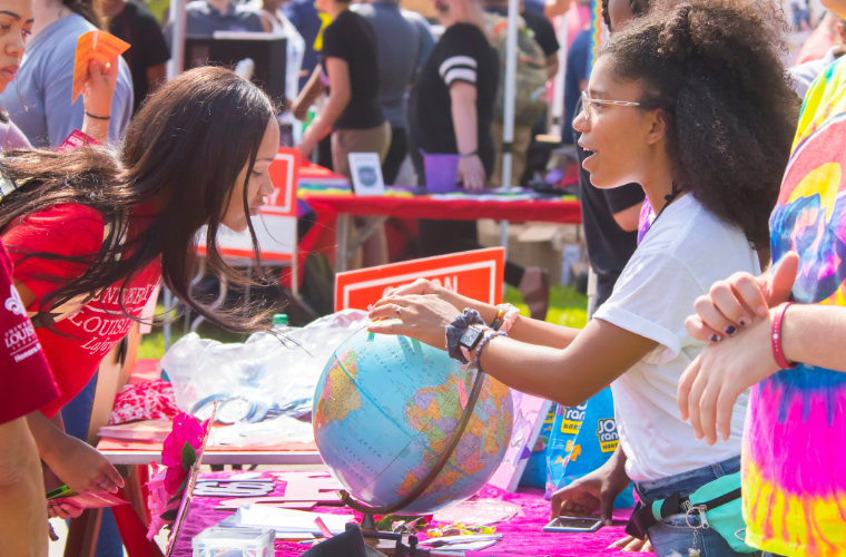 A University of Louisiana at Lafayette campus event booth, where two students discuss a point on a globe.