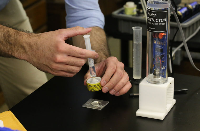 A physics student pushes liquid from a vial into a test tube for a physics research experiment. 