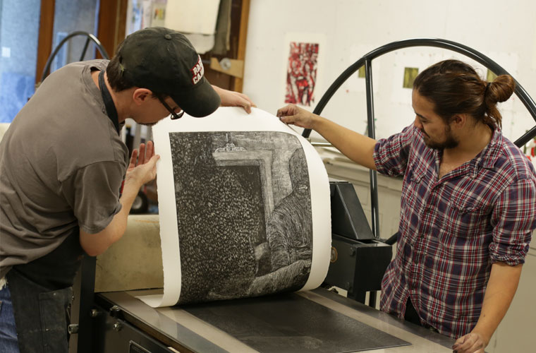 A University of Louisiana at Lafayette visual arts major workings on a printing press with his professor