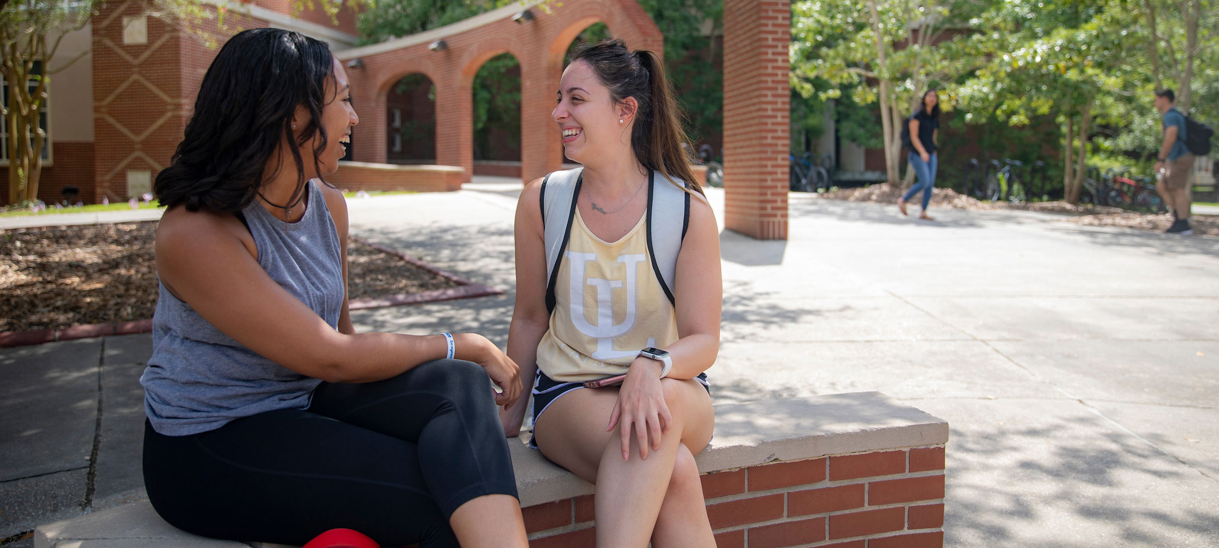 Two University of Louisiana at Lafayette students sit and talk on a bench on campus