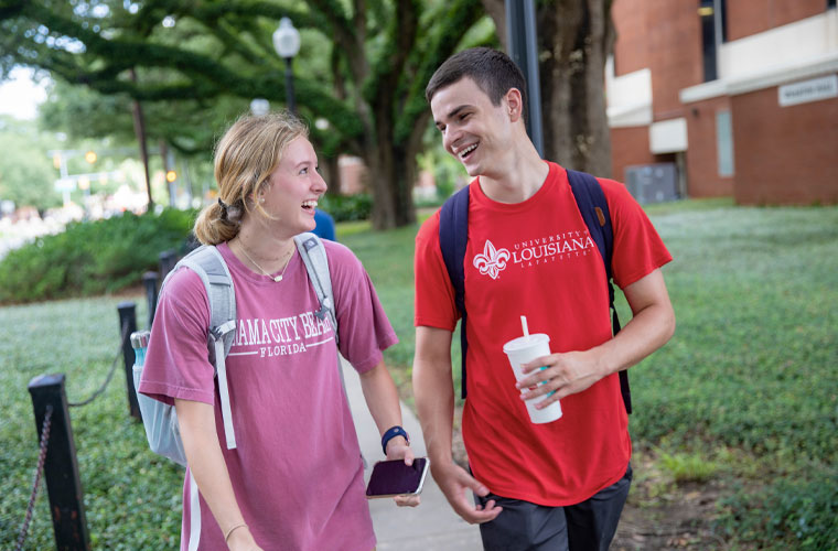 Two University of Louisiana at Lafayette students smiling at each other while walking on campus
