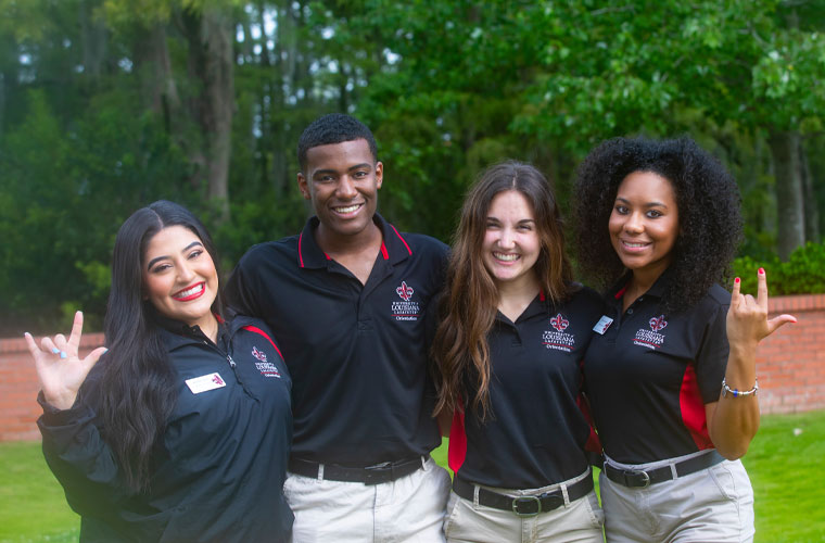 A group of University of Louisiana at Lafayette orientation leader students smiling at the camera and holding up the UL hand sign