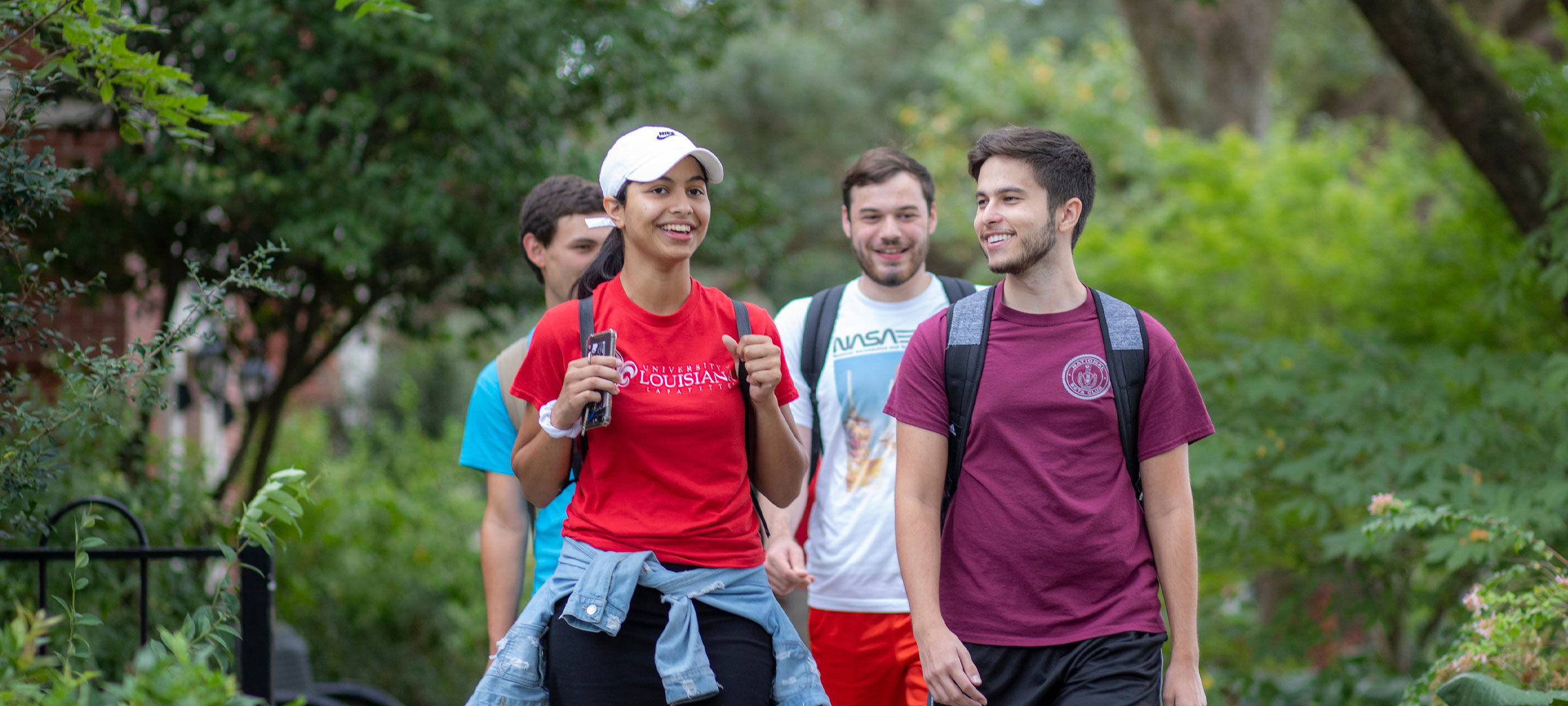 Four University of Louisiana at Lafayette students walk between two rows of gardens on campus