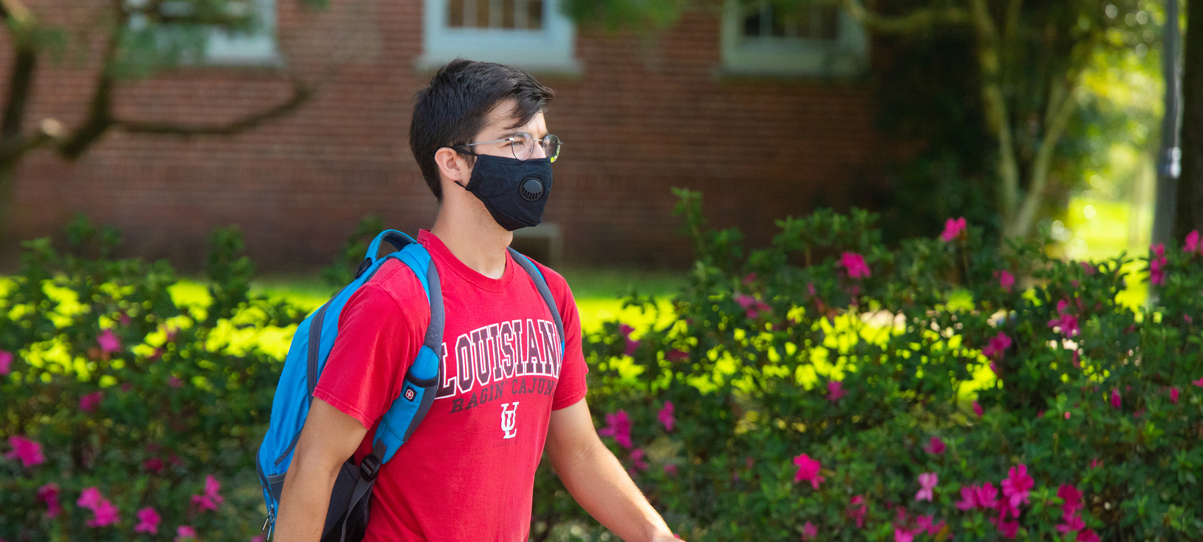 Student walking on UL Lafayette's campus with a mask