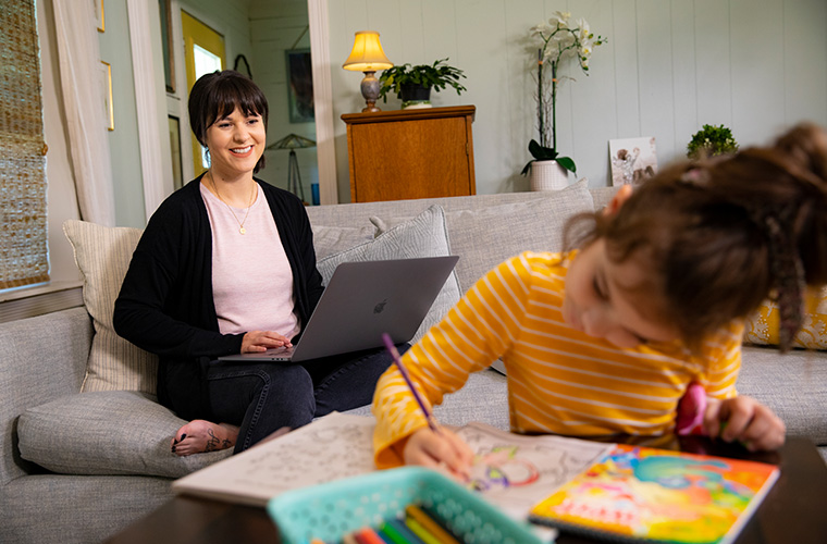 UL Lafayette online student working at a computer at home while her daughter colors.