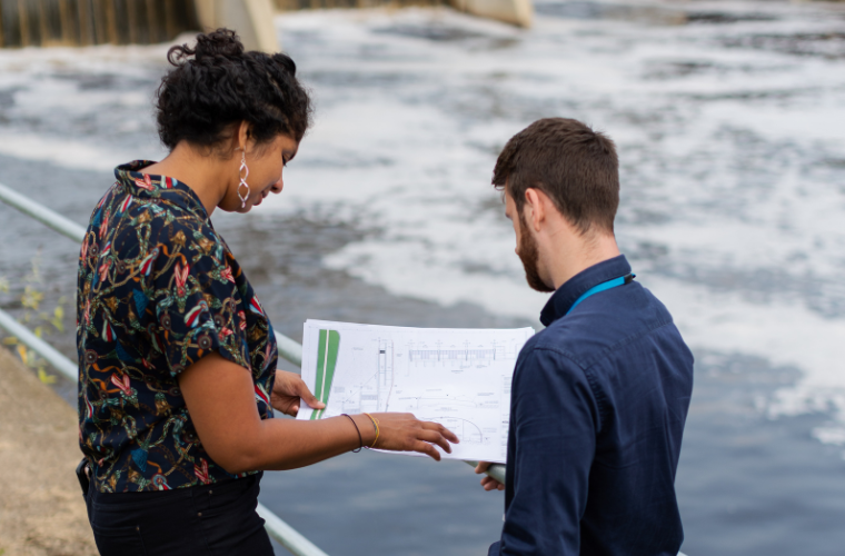 A woman and a man review schematics near a hydraulic dam. 