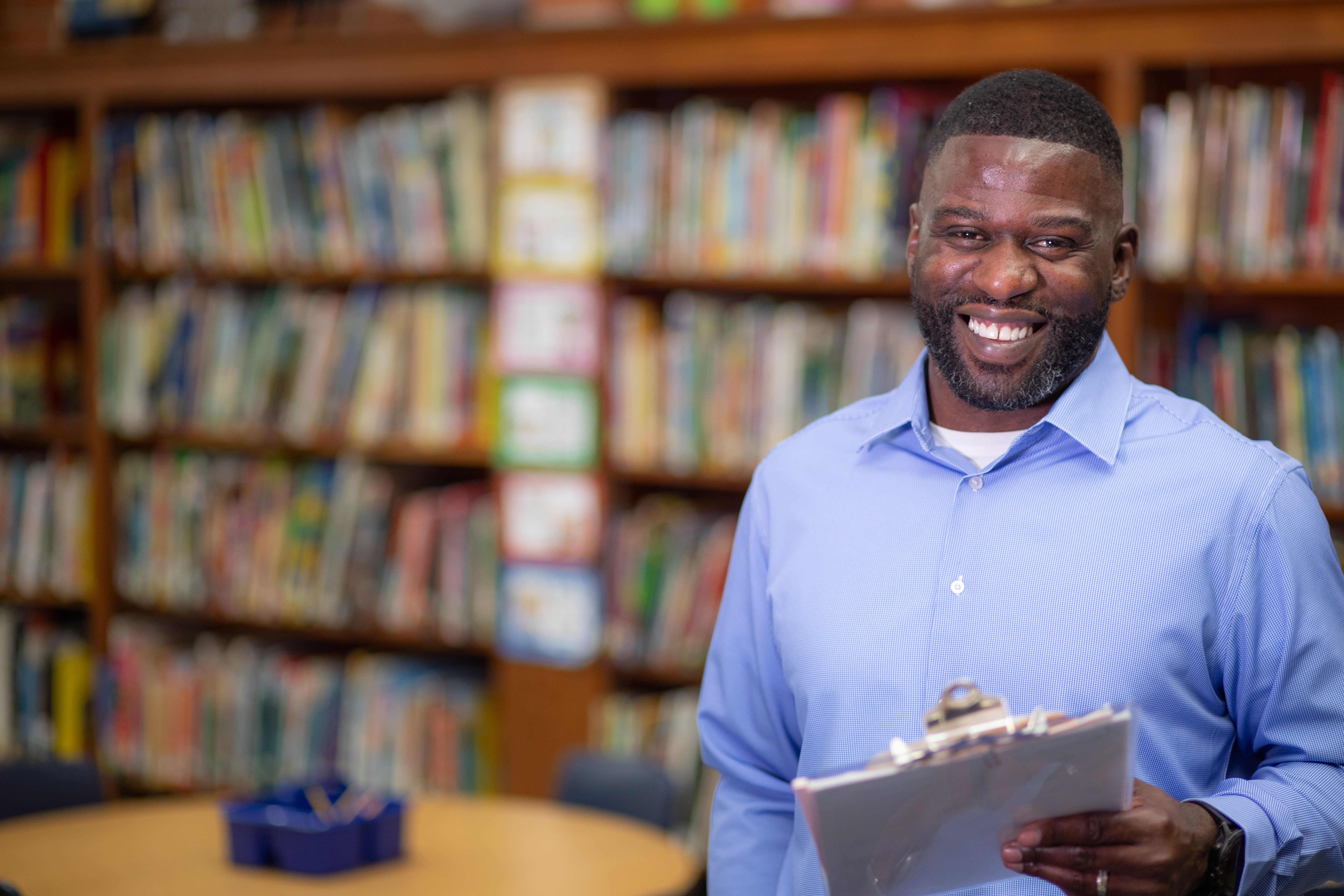 M.Ed. in Educational leadership graduate Kreig Triggs stands in a school library holding a clipboard