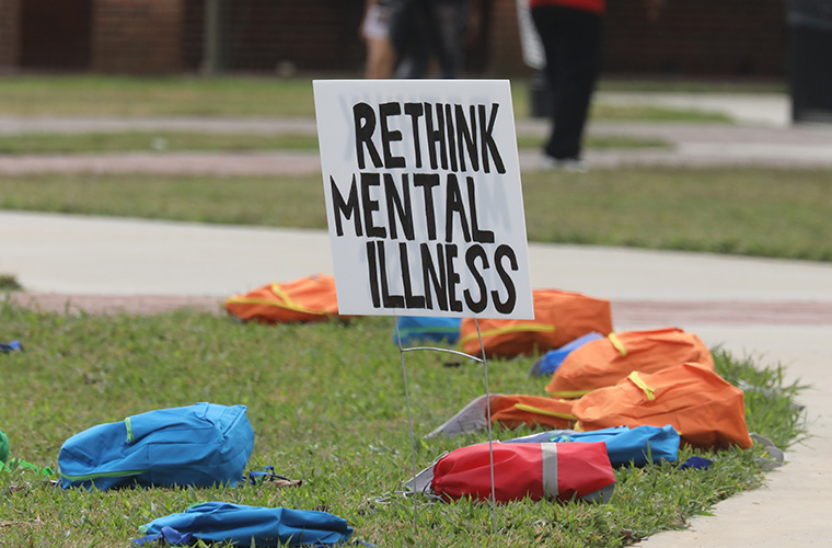 Rethink Mental Illness sign in UL Lafayette Quad surrounded by backpacks for suicide awareness.