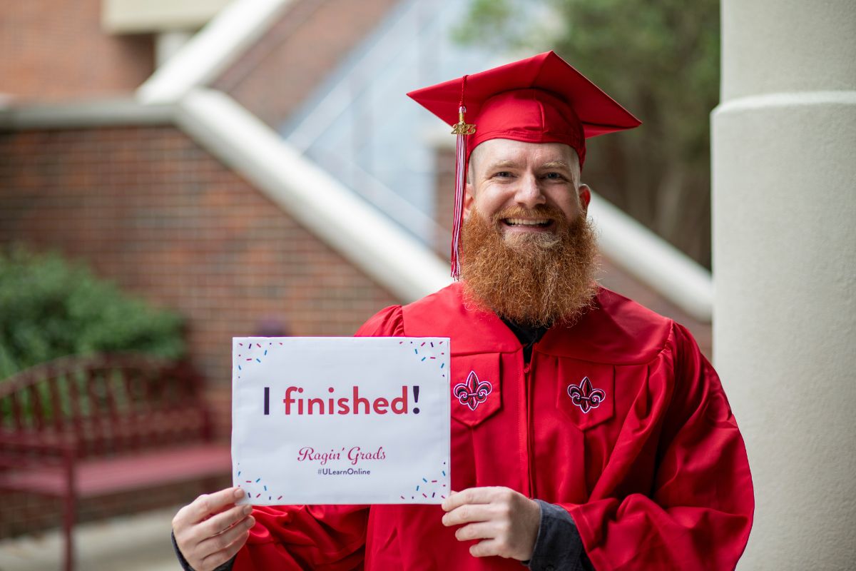 Kail Kidd, clad in his graduation cap and gown, holds a sign that reads, "I finished!"