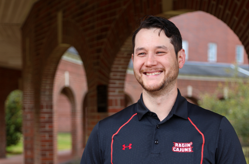 Jonathan Kim, CPA, is pictured on campus in a black, Ragin' Cajuns polo shirt. Kim earned both his bachelor's degree and master's degree at UL Lafayette.