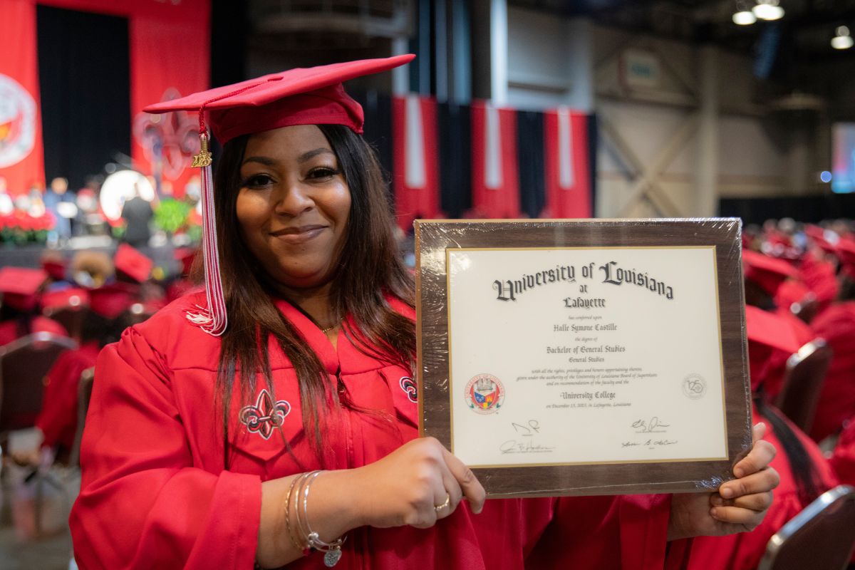 Halle Castille, wearing her graduation cap and gown, holds up her diploma for her Bachelor of General Studies degree from UL Lafayette.