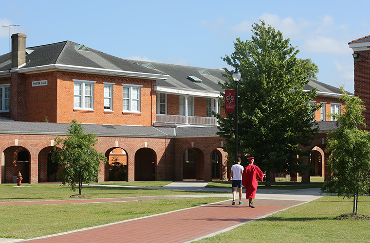 Student in graduation gown walking toward Foster Hall in the Quad.