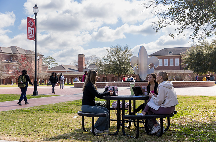UL Lafayette students sitting at a table in the quad on campus.