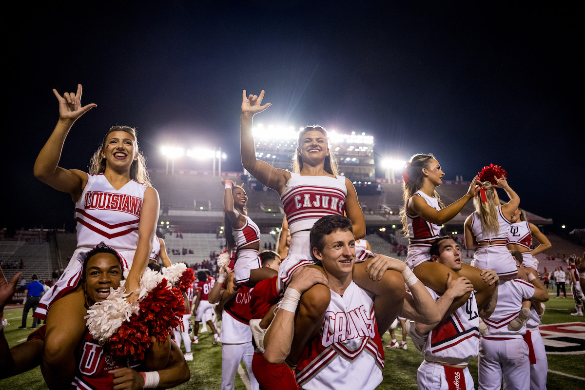Cheerleaders raise their hands in "Geaux Cajuns" signs at an evening homecoming football game at Cajun Field.