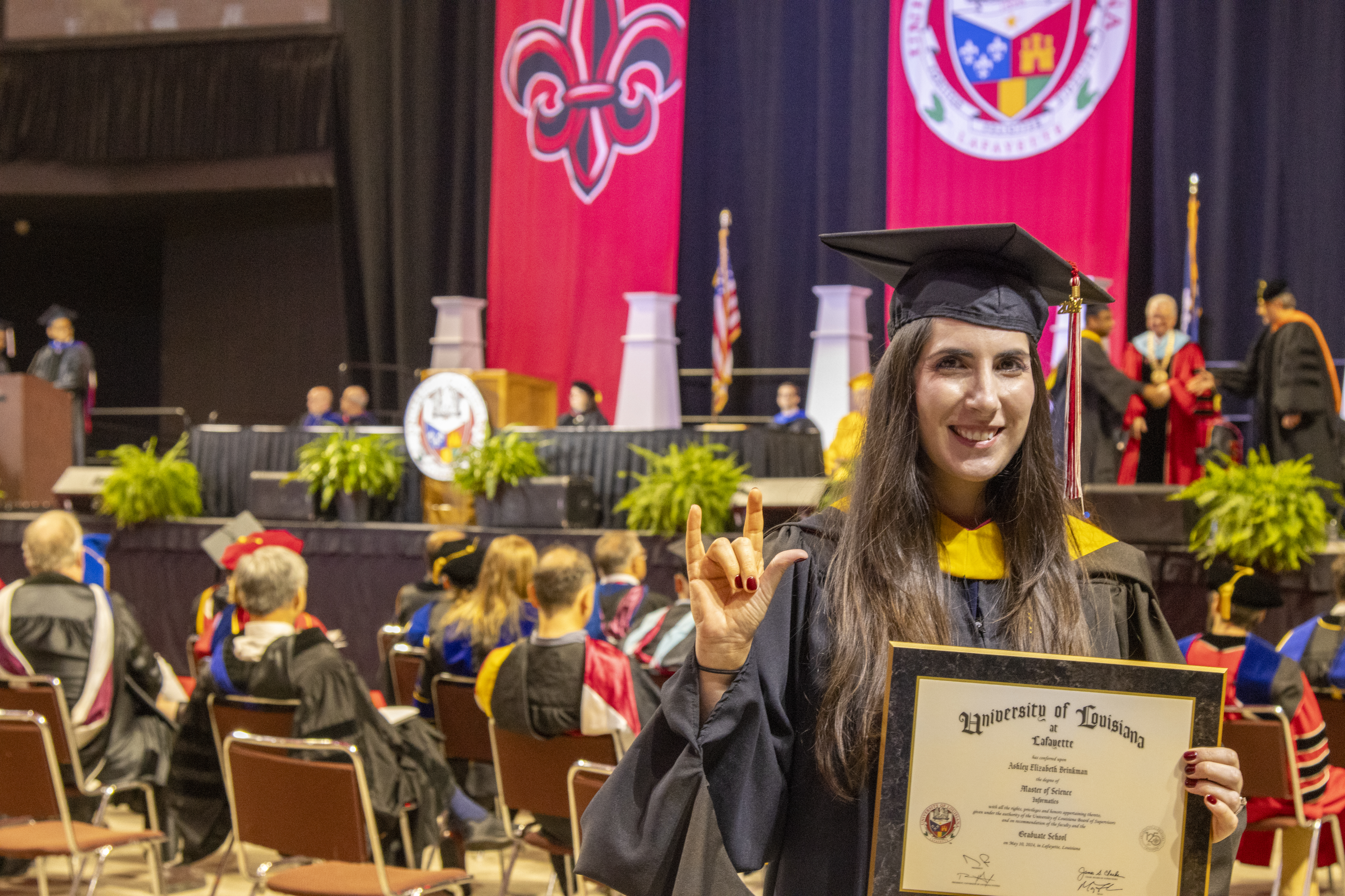Ashley Brinkman holds up the UL Lafayette hand symbol during Spring 2024 commencement ceremonies. Brinkman earned her M.S. in Informatics online.