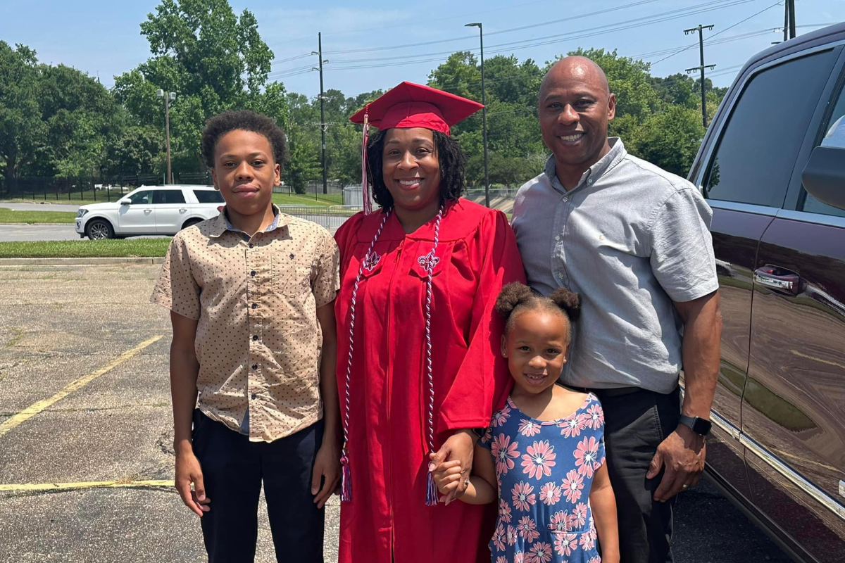 RN to BSN grad Tiffany Woods smiles for photo with husband, son, and daughter in her cap and gown.