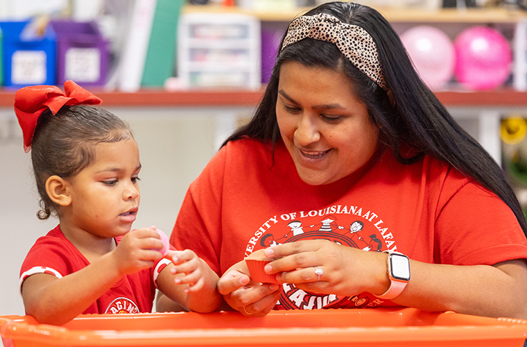 Child Development Center teacher and child playing with sand