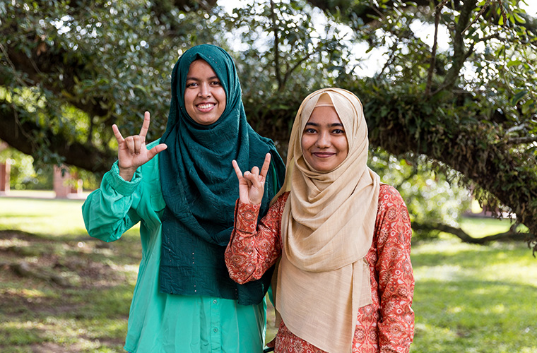 Two UL Lafayette international students in front of an oak tree on campus