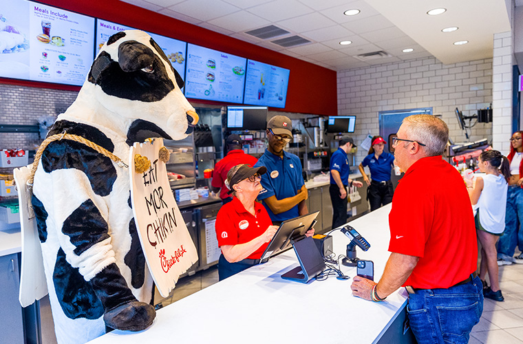 Chik fil a cow mascot with "Buy more chicken" sign at the on campus location of Chik fil a.