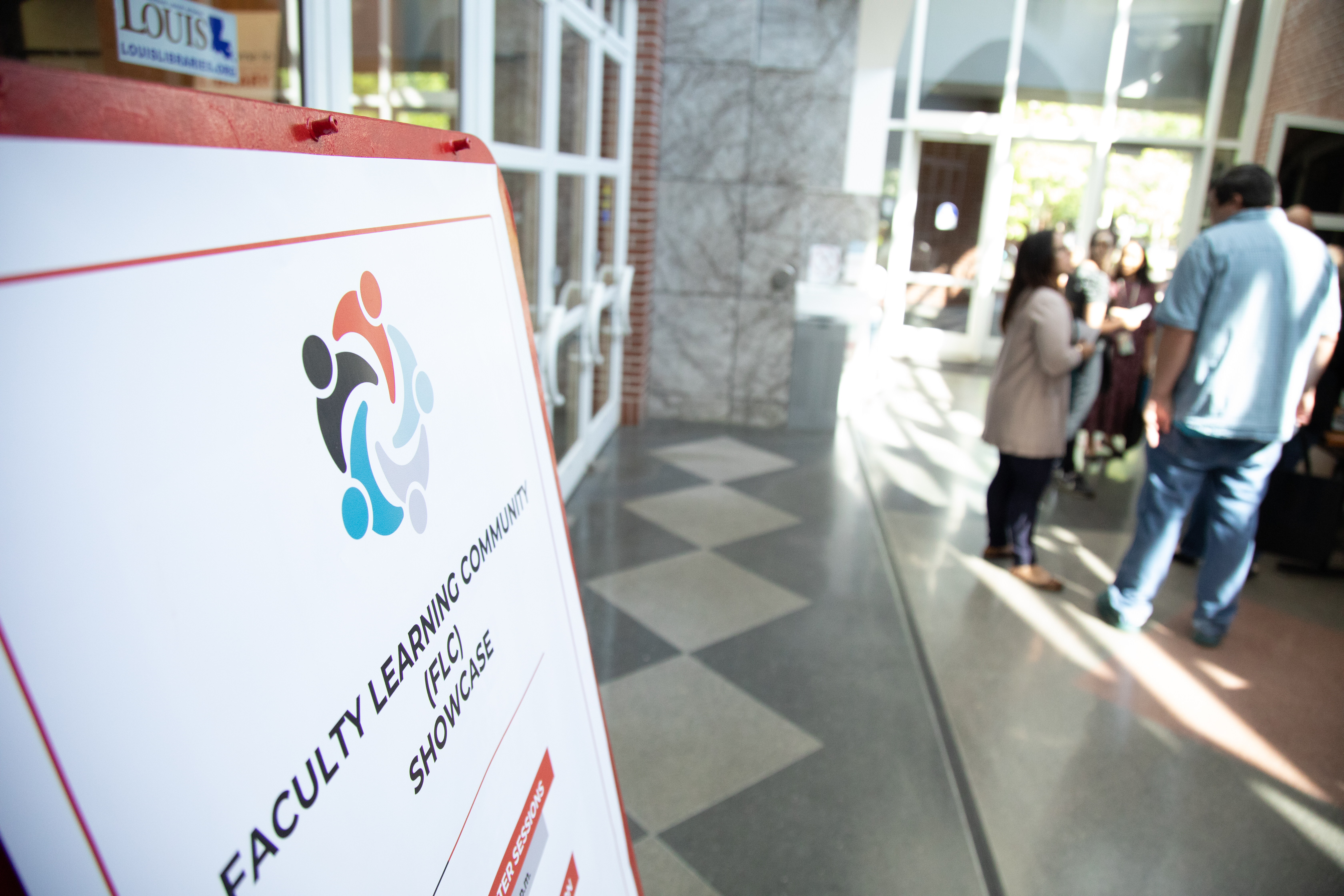 A sign for the Faculty Learning Community Showcase is pictured in the foreground with participants seen milling in the background.