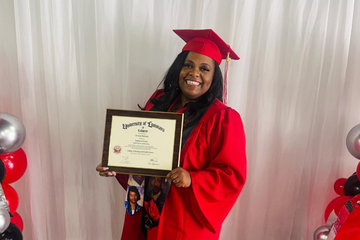 Health Services Administration online graduate smiles in cap and gown while holding her newly conferred bachelor's degree. 