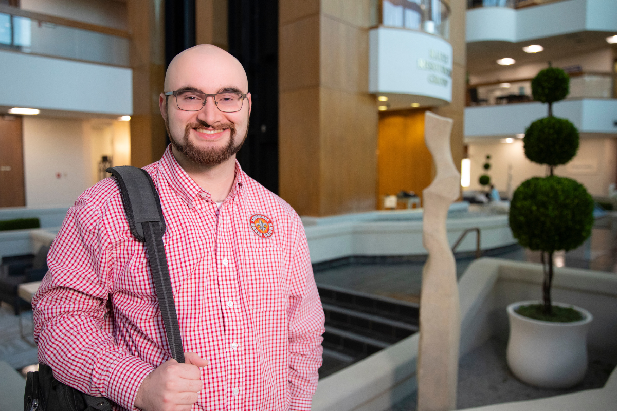 Online M.S. in Accounting alumni Seth Prather smiles in an office setting, wearing a red UL Lafayette button-down and shoulder bag.