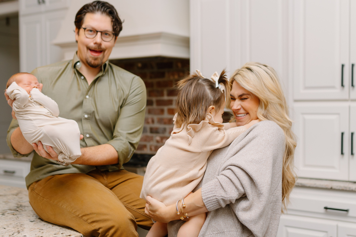 Online MBA grad Victoria Alleman smiles in kitchen with her babies and husband.