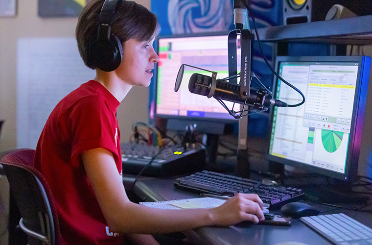 Radio host sits at a microphone and computer