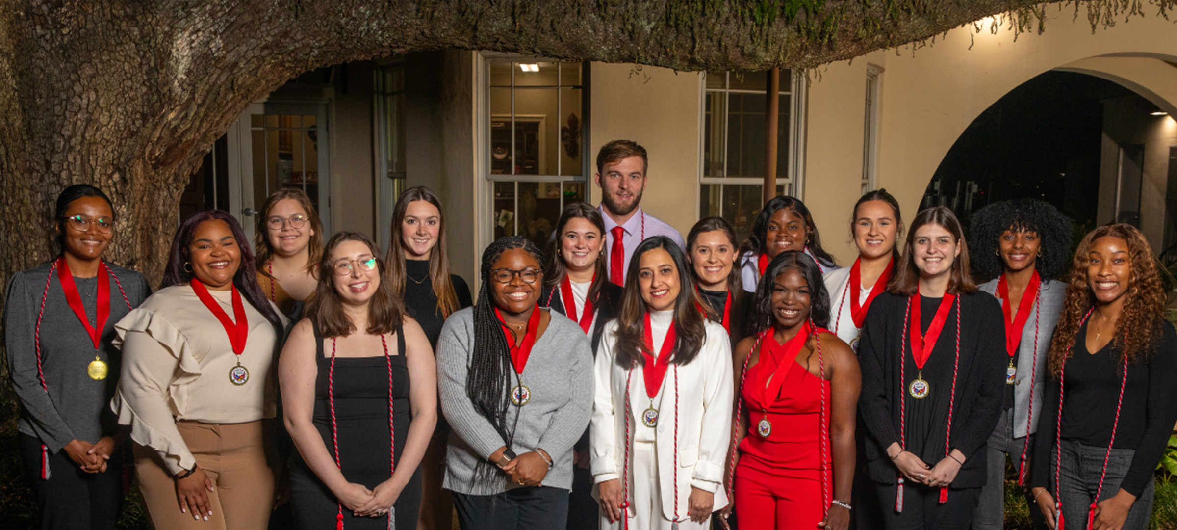Group of UL Lafayette students wearing cords and medals under an oak tree