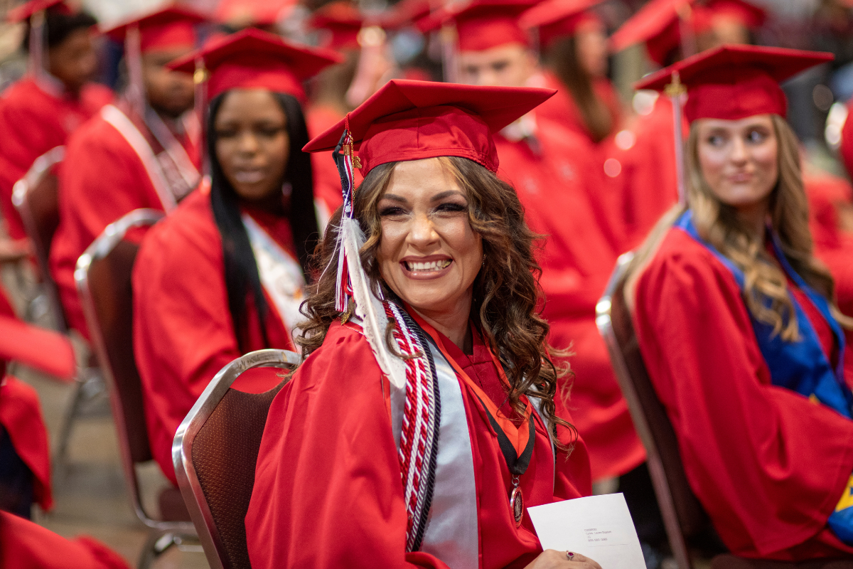 Online General Studies graduate smiles in cap and gown while seated at UL Lafayette's commencement ceremony.