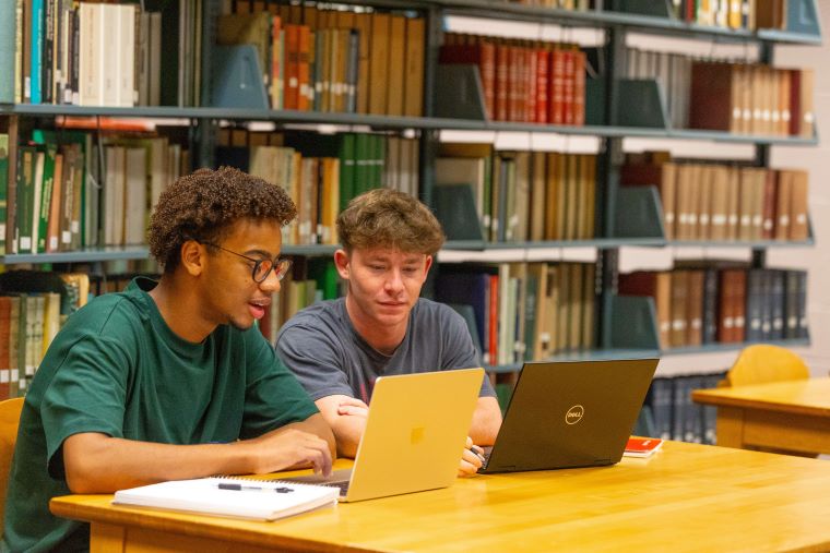 Two students work on laptops in the library 