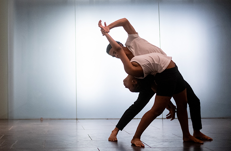 Two UL Lafayette dance students share a moment of movement in front of a white background