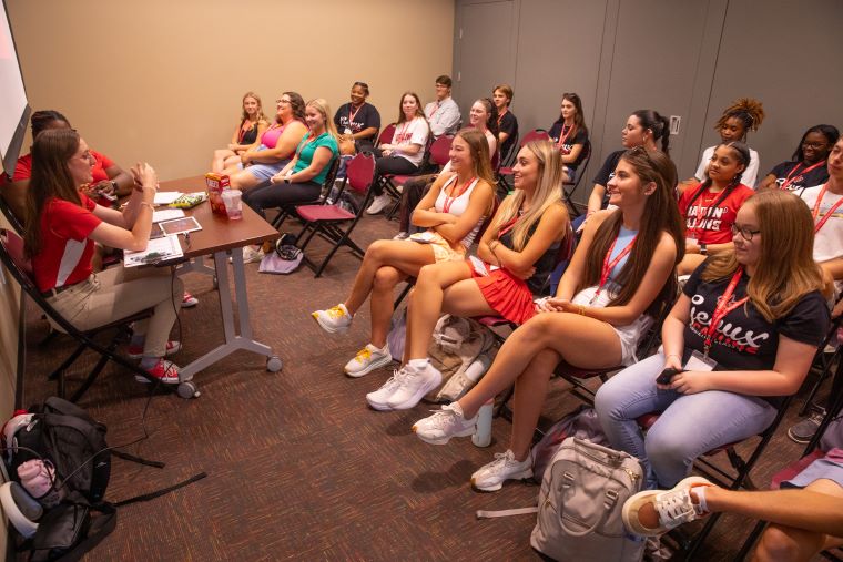 Two Orientation Leaders in red polos sit at the front of a classroom, speaking to a group of new students at Orientation