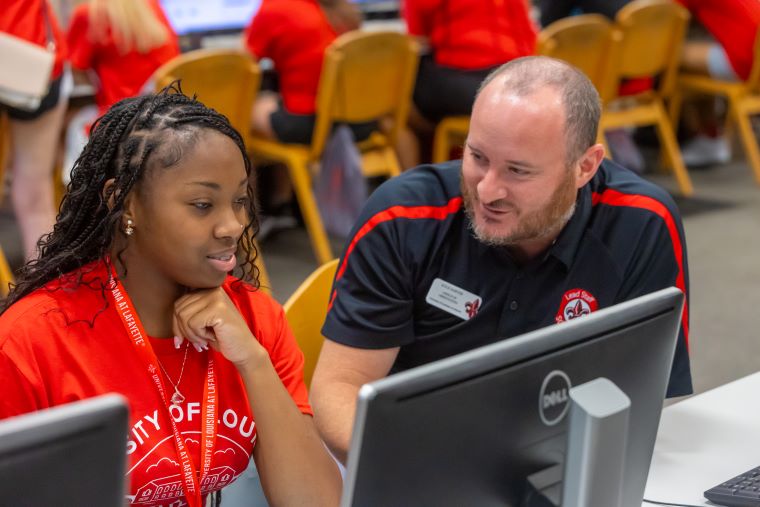 A UL Lafayette staff member assists an Orientation attendee registering for classes in a computer lab