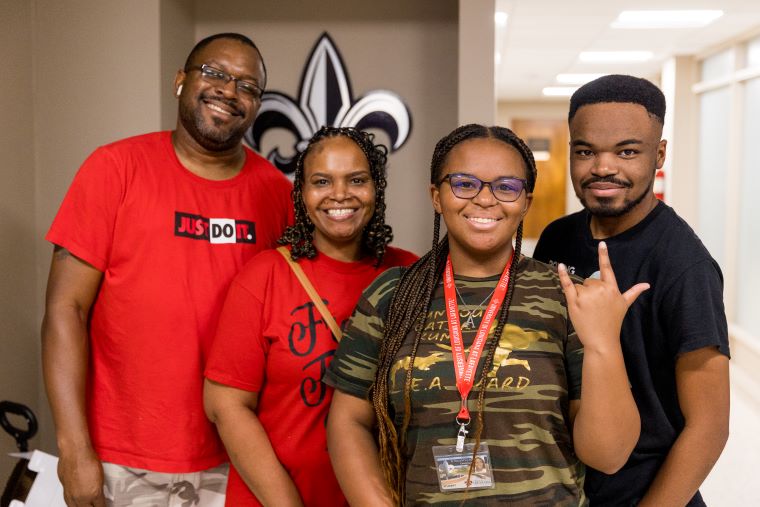 A student and her family pose in front of a fleur de lis sign
