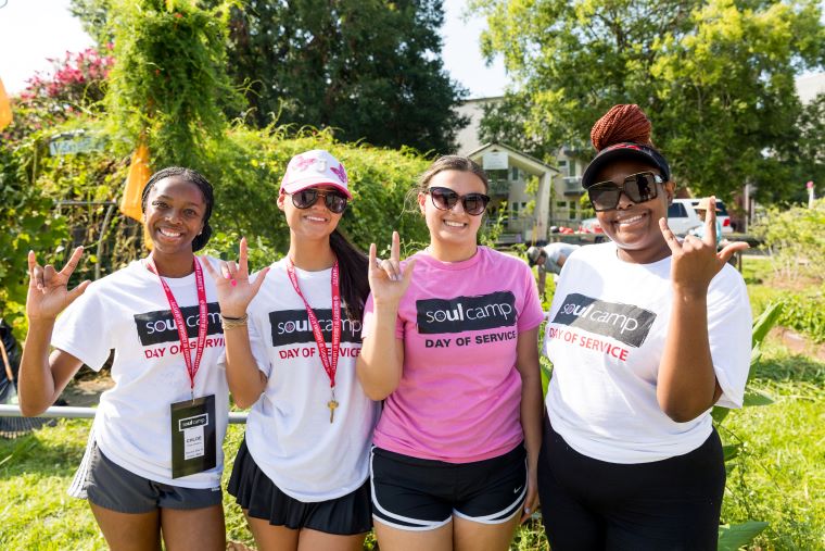 Four students wearing SOUL Camp t-shirts pose in a garden, giving the UL hand sign