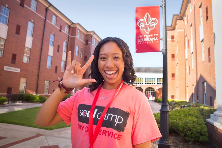 A student in a SOUL Camp shirt poses while displaying the UL hand sign