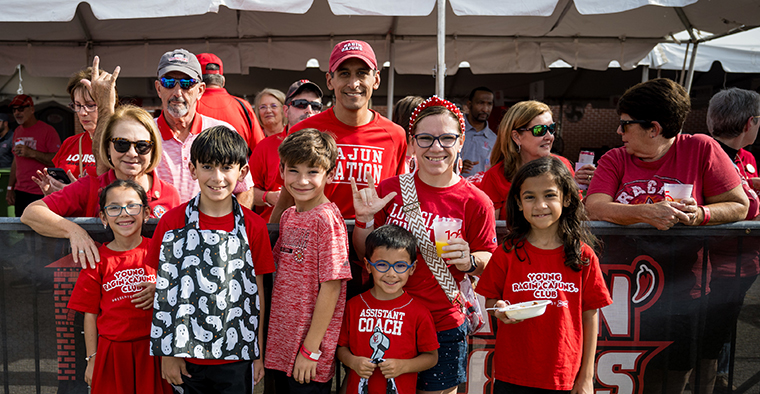 Family wearing UL Lafayette Ragin' Cajuns gear pose in front of the Alumni tent before the homecoming football game