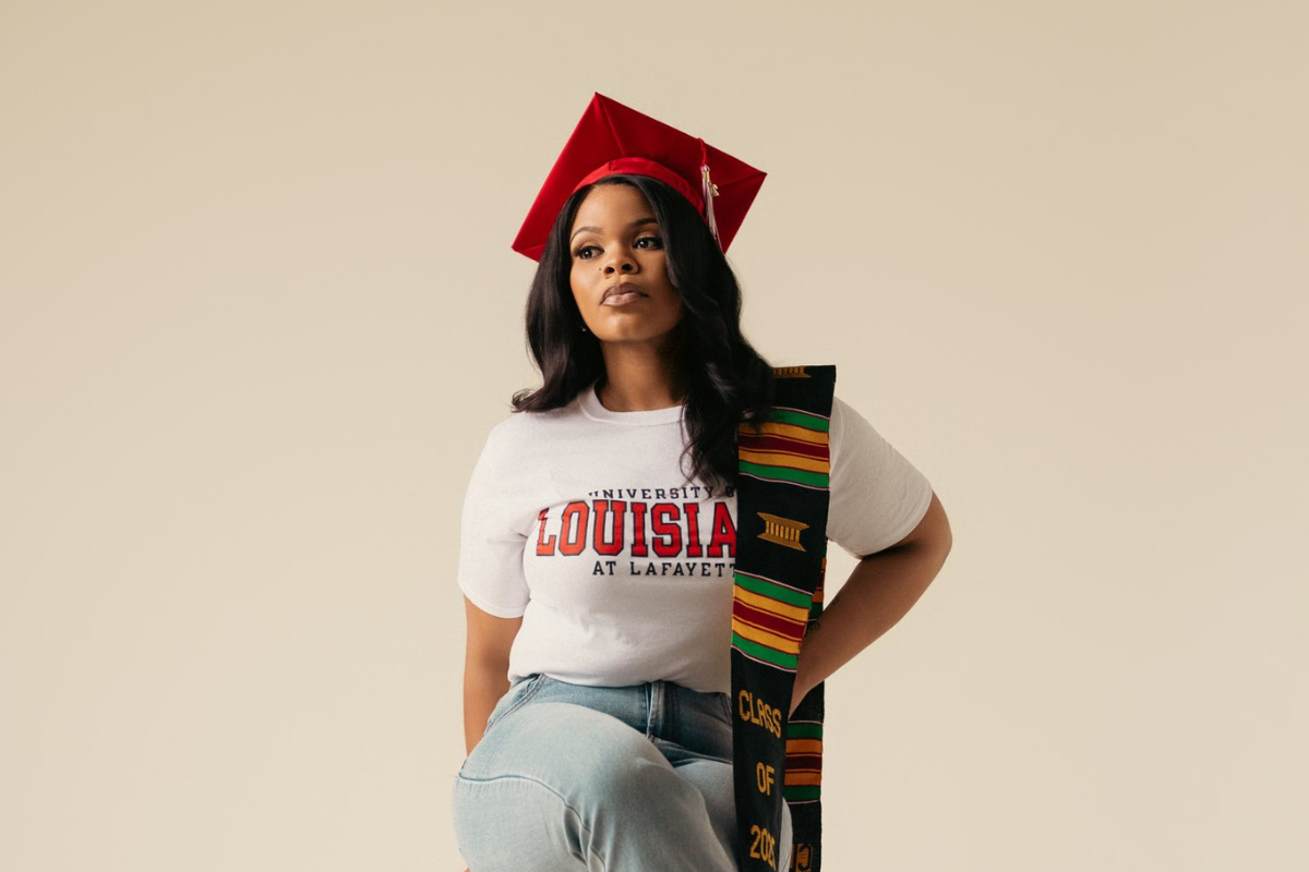 Chanoah Smith poses for photo wearing a white UL Lafayette t-shirt and red graduation cap after completing the management degree online program.