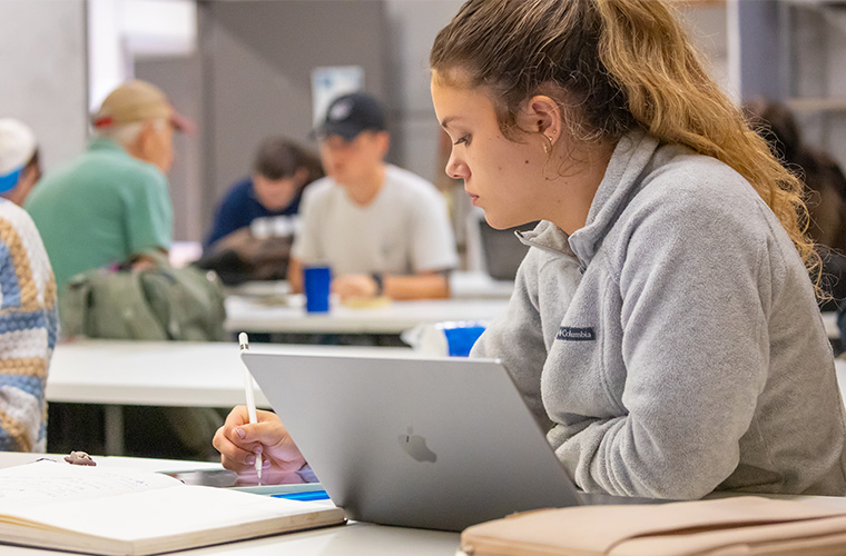 UL Lafayette graphic design student in class working on their tablet with a laptop open on their desk.