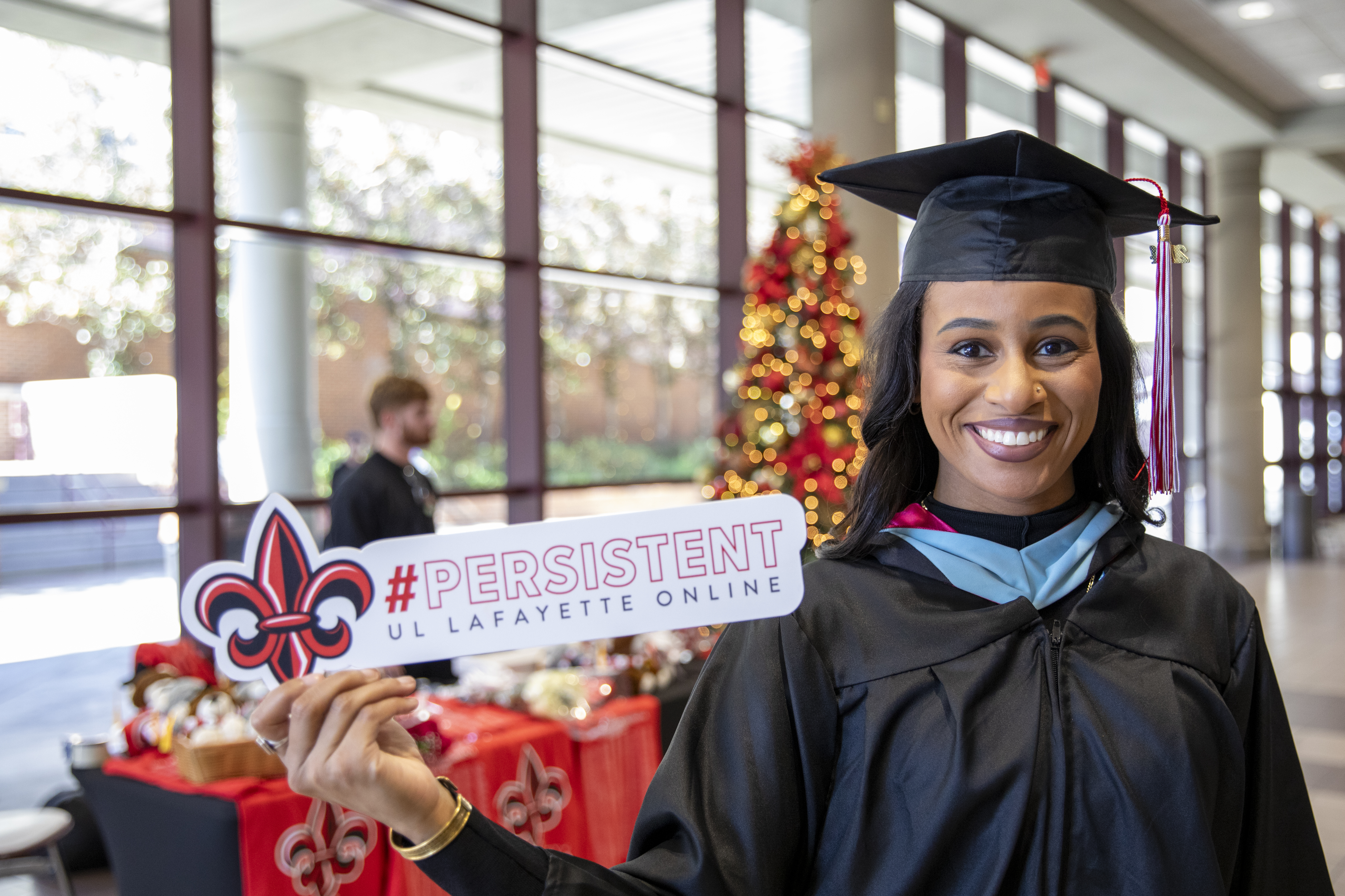 Graduate of the online Master of Education program smiles at commencement while holding a sign that reads "#Persistent"