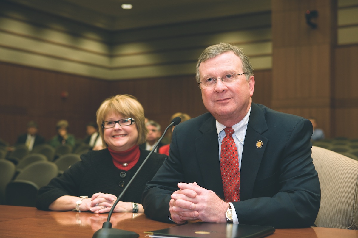 Dr. Joseph and Gail Savoie sit behind a microphone at a podium.