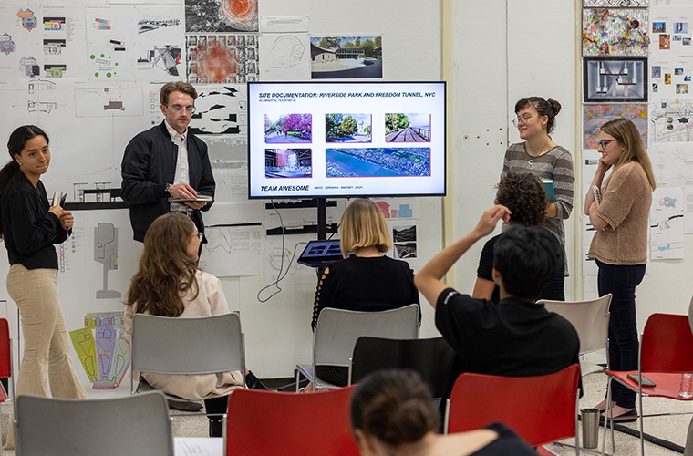 UL Lafayette Master of Architecture students giving a presentation to their classmates on a slide titled "SITE DOCUMENTATION: RIVERSIDE PARK AND FREEDOM TUNNEL, NYC"