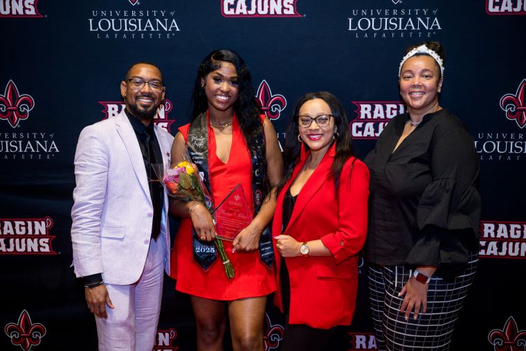 An LEP student wears a graduation stole and poses with LEP staff advisors at an event